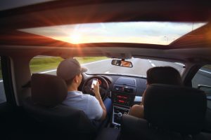 image of couple driving in vehicle; driver has his phone out 