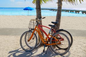 Key West injury lawyer on e-bike accidents; two bicycles resting next to two palm trees on a sandy beach overlooking turquoise water